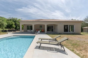A modern house with a swimming pool, outdoor seating, and a patio.