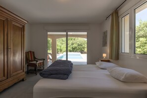 A bedroom with a bed, a chair, a wardrobe, and a view of a swimming pool.