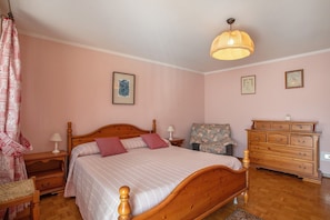 A bedroom with a wooden bed, a nightstand, a dresser, a chair, and a hanging light fixture.
