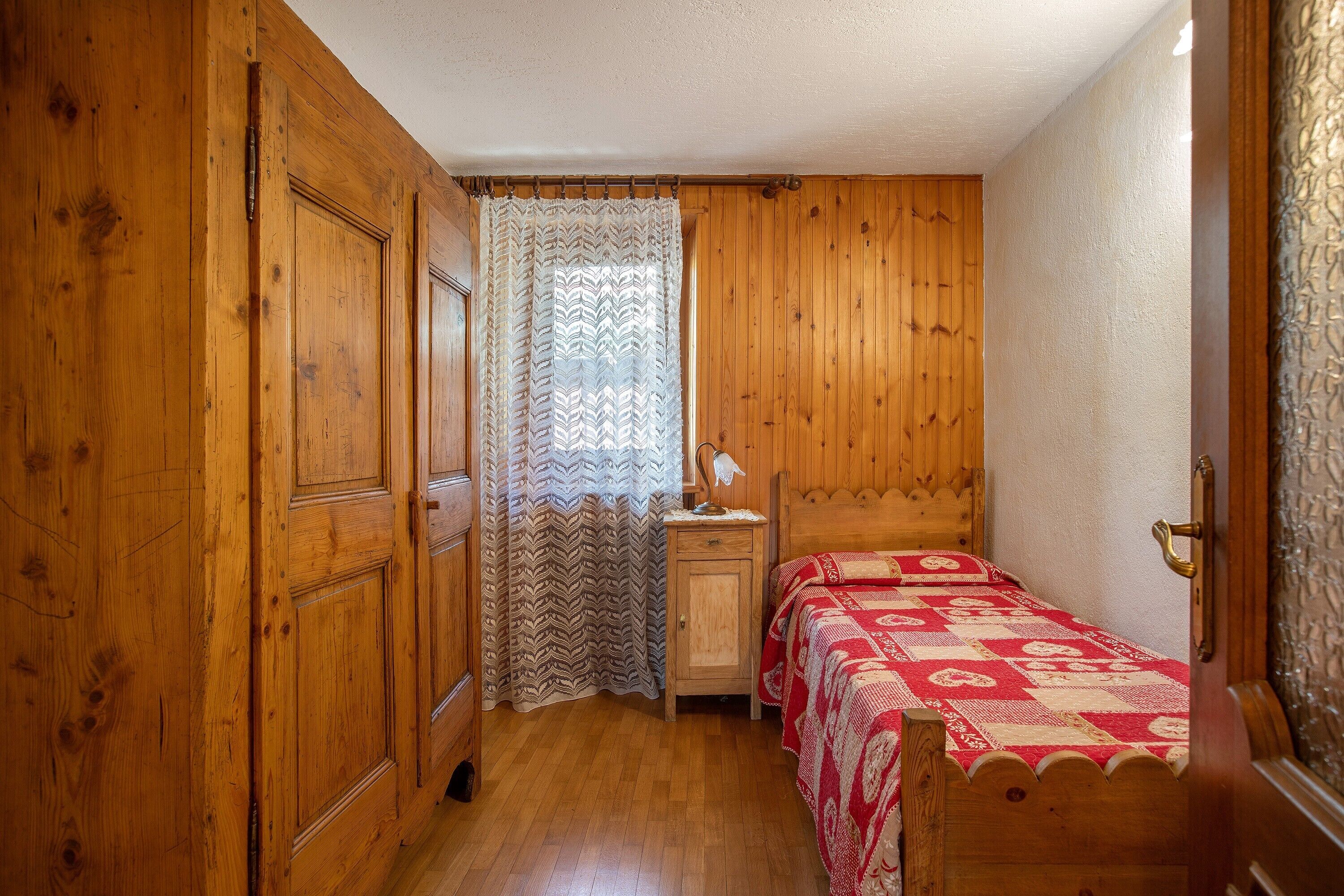 Una stanza con pannelli di legno, un letto, un comodino e una finestra con tenda decorata.