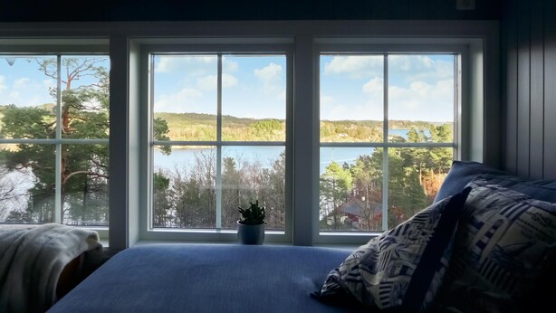 A bedroom with a large window offering a view of a lake and forest. - Lovely home in Høvåg with WiFi (Høvåg)