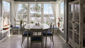 A dining room with a round table, white chairs, and a view of a lake through large windows. - Lovely home in Høvåg with WiFi (Høvåg)