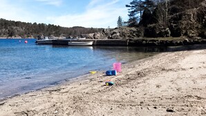 A sandy beach with a calm lake, boats docked, and a rocky shoreline. - Lovely home in Høvåg with WiFi (Høvåg)