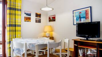 Et spiseområde med et bord, stole, en lampe, et fjernsyn og kunst på væggen.