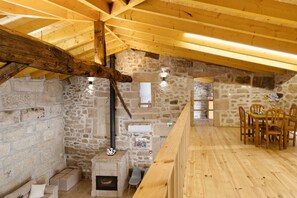 Une pièce rustique avec des murs en pierre, un plafond en bois, une cheminée, une table à manger avec des chaises et un banc en bois.
