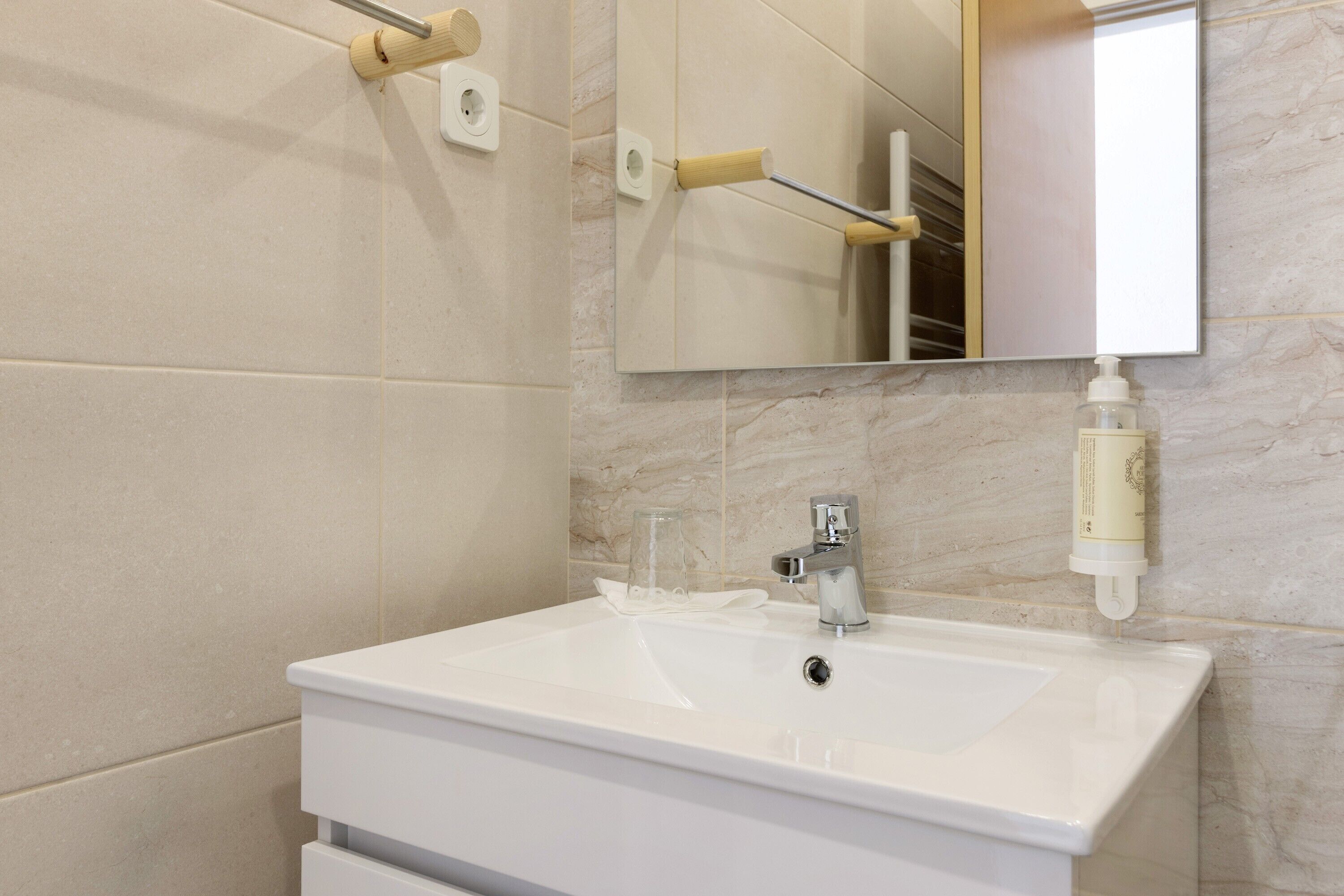 Un bagno con un lavandino bianco, uno specchio e un erogatore di sapone.