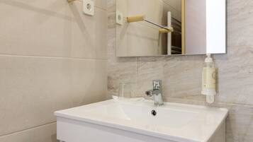 Un bagno con un lavandino bianco, uno specchio e un erogatore di sapone.