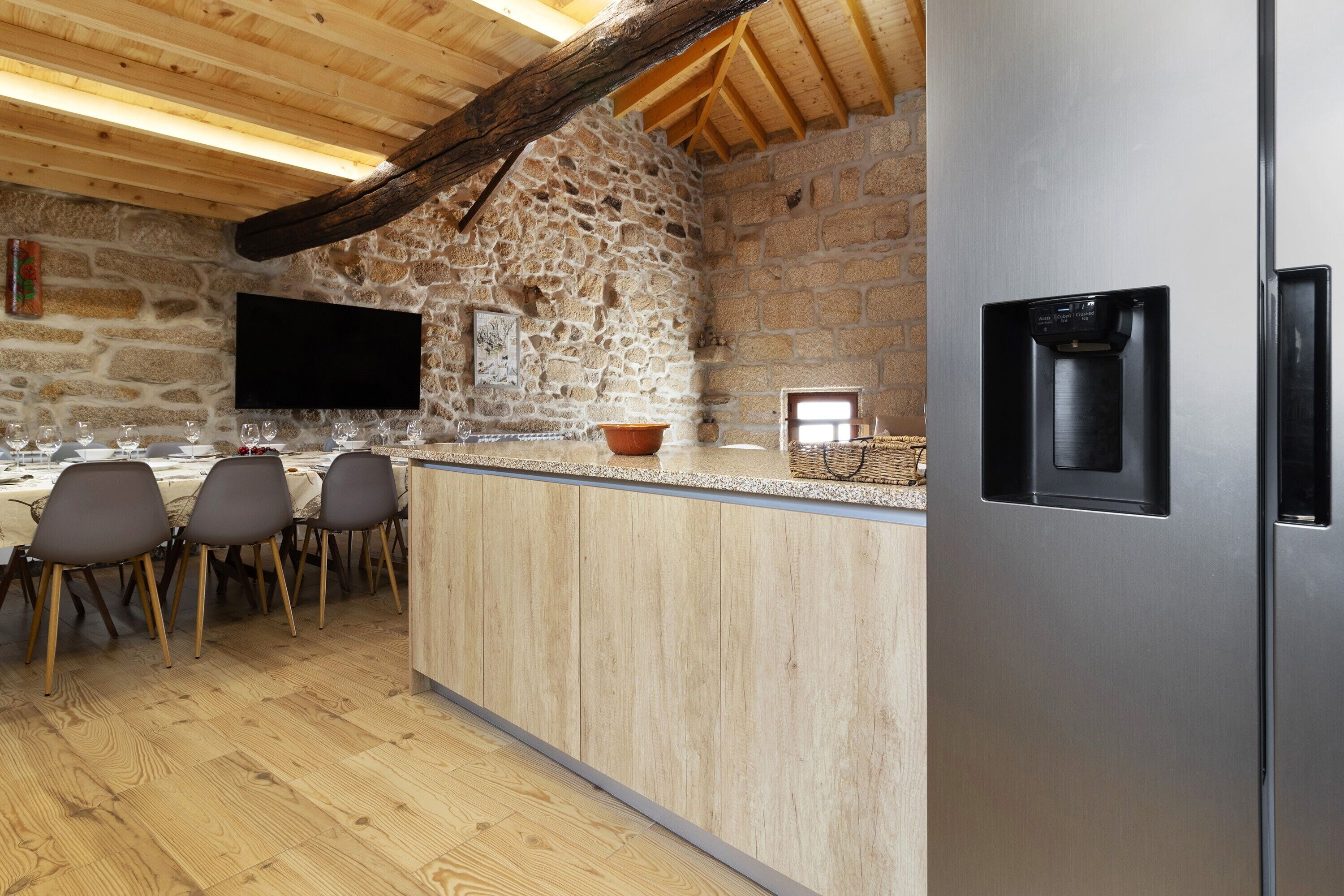 A kitchen with a stone wall, wooden ceiling, and a stainless steel refrigerator.
