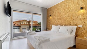 Een slaapkamer met een groot bed, een houten wand, een aan de wand bevestigde televisie en uitzicht op het buiten.