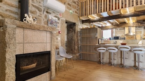 Een keuken met stenen muren, voorzien van een open haard, witte stoelen en een bar met krukken.