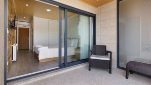 A modern hotel room with a sliding glass door, a bed, a chair, and a bench.