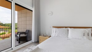 A hotel room with a bed, a nightstand, a chair, and a view of the outdoors.