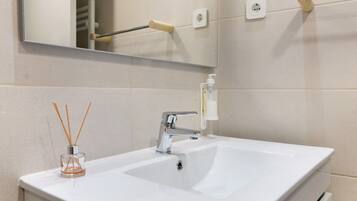 A bathroom with a white sink, a mirror, a towel rack, and a soap dispenser.
