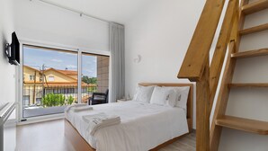 A bedroom with a large bed, a wooden ladder, a sliding glass door, and a view of buildings outside.
