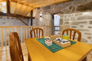 Een houten eettafel met stoelen, een gezelschapsspel en een groene placemat in een kamer met stenen muren en houten balken.