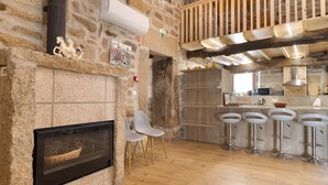 A stone-walled room with a fireplace, white chairs, and a kitchen area with bar stools.