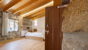 Ein Schlafzimmer mit Steinwand, Holzbalkendecke, einem Bett und einem Kleiderschrank.