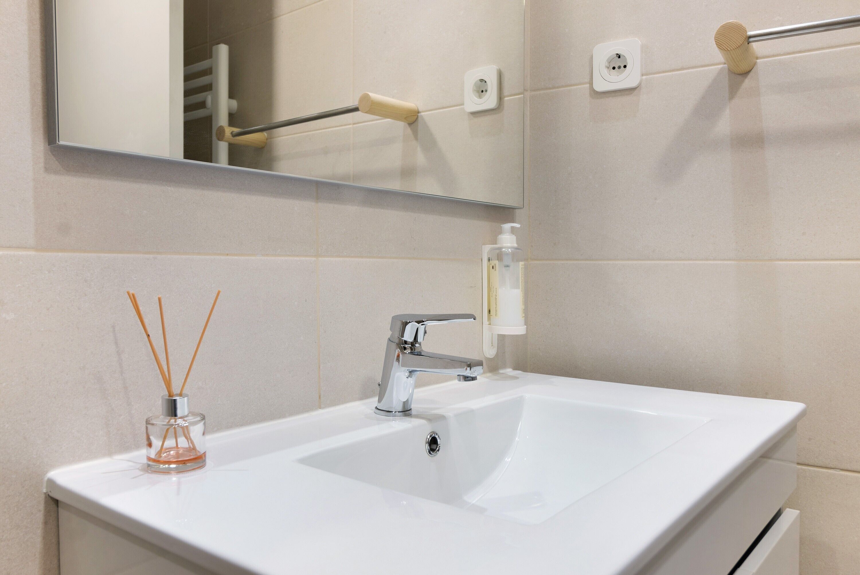 A bathroom with a white sink, a mirror, a towel rack, and a soap dispenser.