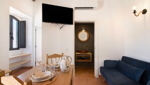 Un comedor con una mesa dispuesta para cuatro personas, un televisor montado encima y un sofá en el área de estar contigua.