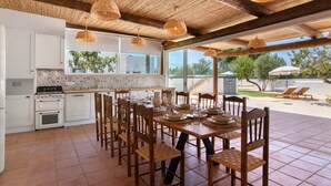 Una cocina con armarios blancos, una estufa y un comedor con sillas de madera y una mesa preparada para cuatro personas.