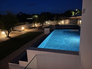 A swimming pool with a clear blue water surface, surrounded by a well-lit patio area with a modern architectural design.