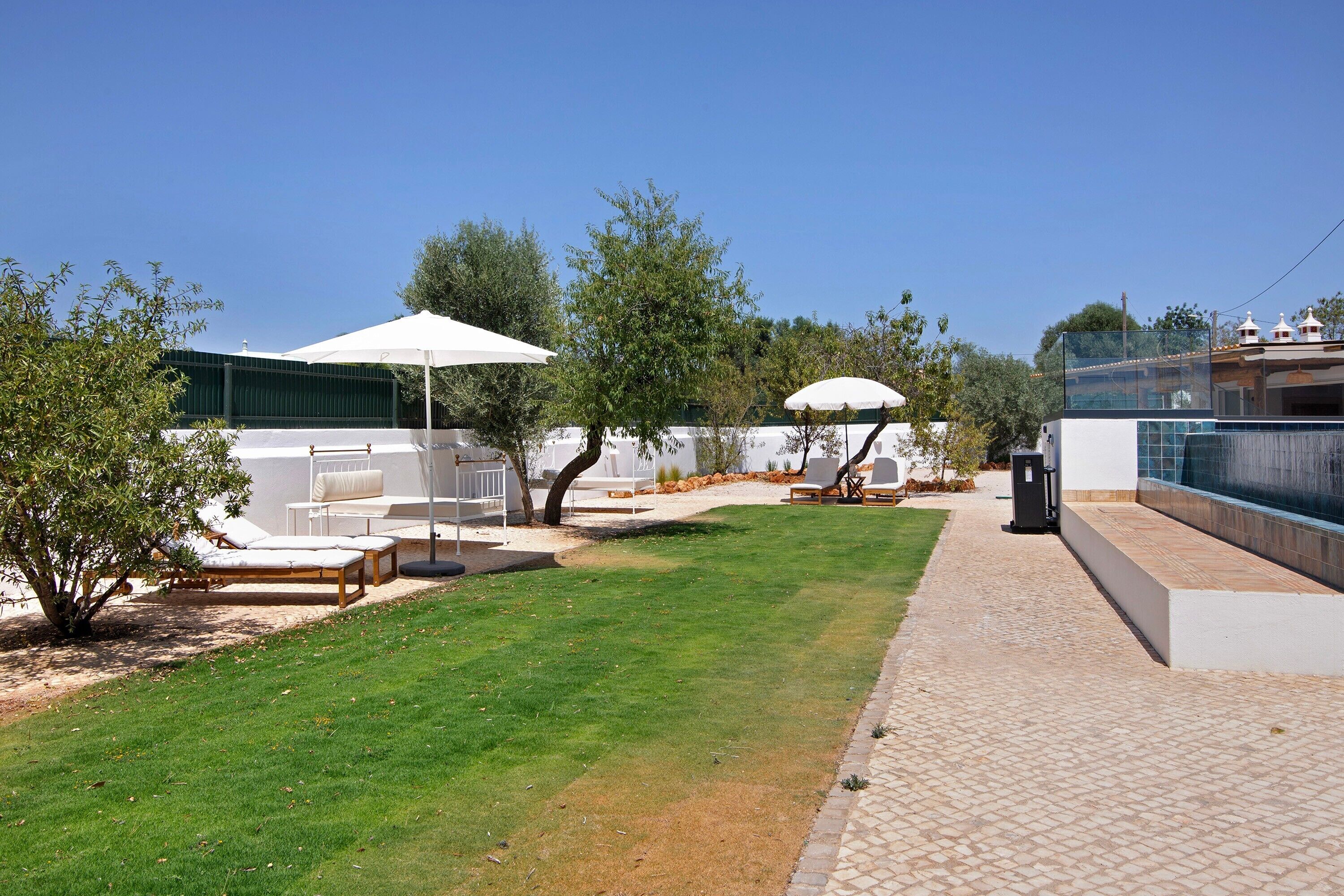 A backyard with a lawn, outdoor furniture, and umbrellas.