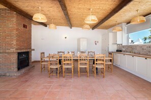 A dining area with a brick fireplace, wooden chairs, and hanging wicker lamps.