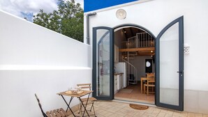 En moderne bygning med en terrasse, et bord og stole, en trappe til et øvre niveau samt en stor glasdør.