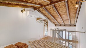 Et soveværelse med træloft, en seng med ternet dynebetræk og udsigt til en balkon.