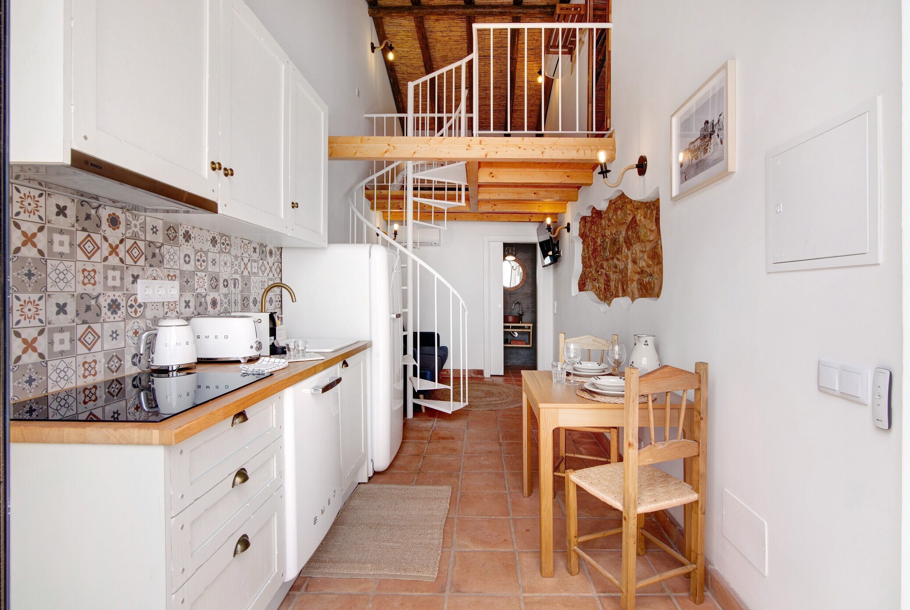 A kitchen with a built-in espresso machine, a wooden dining table, and a spiral staircase.