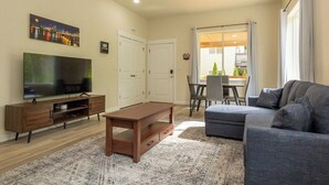 A living room with a flat-screen TV, wooden entertainment unit, grey sofa, and patterned rug. - Lovely Condo close to town with Forest View (Longview)