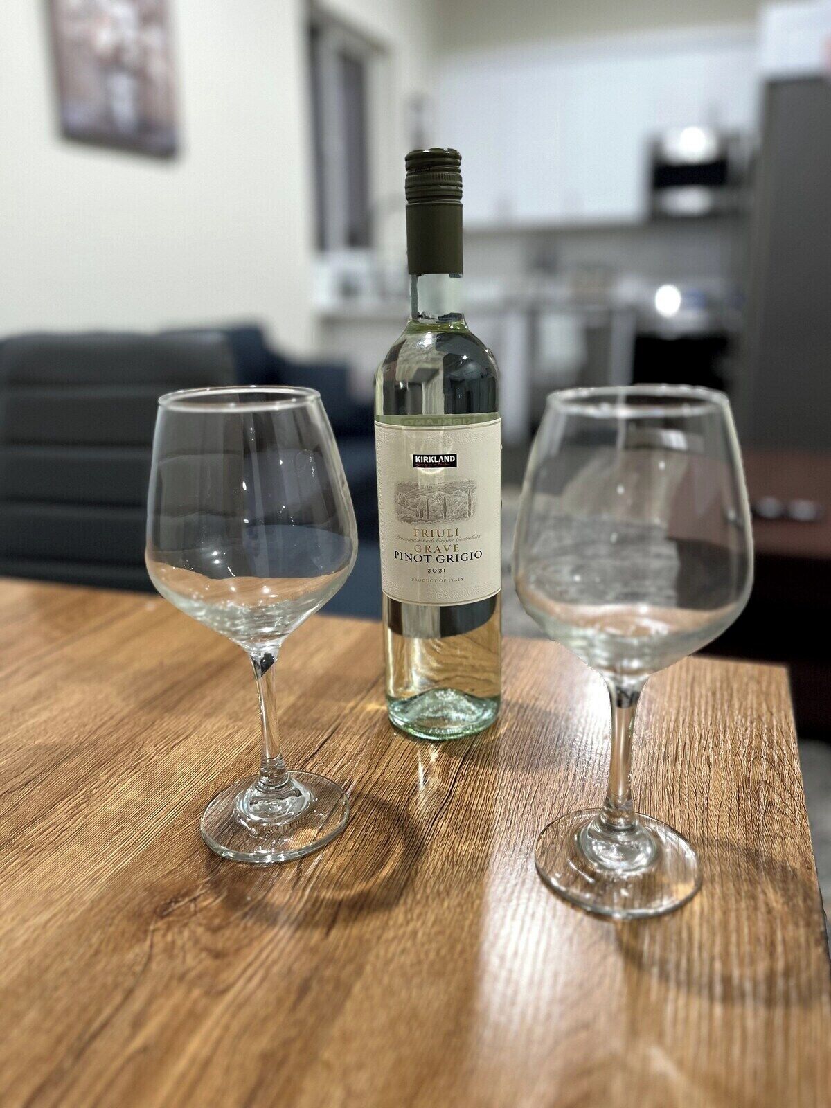 A bottle of Friuli Grave Pinot Grigio 2021 on a wooden table with two empty wine glasses.