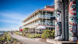 A waterfront building with a balcony, outdoor seating, and totem poles. - Lovely Condo close to town with Forest View (Longview)
