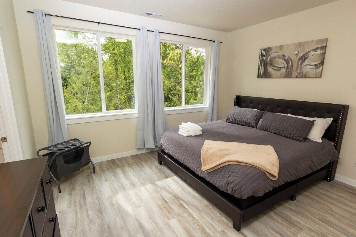 Une chambre à coucher avec un grand lit, une fenêtre avec des rideaux, une tête de lit et une œuvre d’art accrochée au mur.