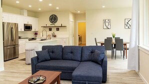 A modern living room with a sectional sofa, a wooden coffee table, and a dining area with a table and chairs. - Beautiful 4 bedroom house with King beds, Forest View (Longview)