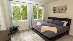 A bedroom with a large bed, a window with curtains, a headboard, and a wall-mounted artwork. - Spacious home and lower level condo with outside entrance. (Longview)