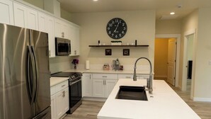 A modern kitchen with white cabinetry, stainless steel appliances, a central island with a sink, and a wall-mounted clock. - Spacious home and lower level condo with outside entrance. (Longview)