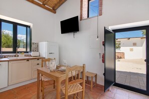 Una cocina con una mesa de comedor, sillas, un televisor y vistas a través de una puerta abierta.