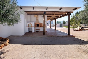 An outdoor patio with a brick oven, wooden pergola, and a white wall. - Apartment 'Monte Gerações 2' with Shared Pool, Wi-Fi and Air Conditioning (Almancil)
