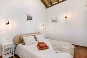A bedroom with a bed, two bedside tables, wall-mounted light fixtures, and framed pictures on the wall.