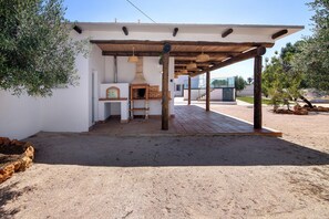 An outdoor patio with a brick oven, wooden pergola, and a white wall.