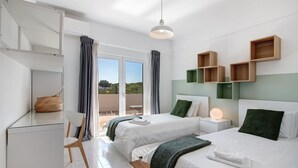 A modern hotel room with two beds, a desk, a chair, and a balcony with a view.