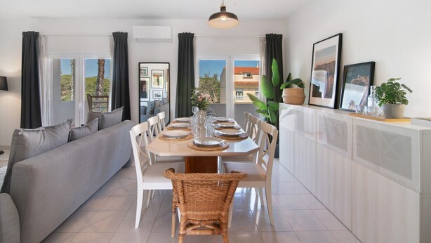 A modern dining area with a sofa, dining table, chairs, and a hanging light fixture.