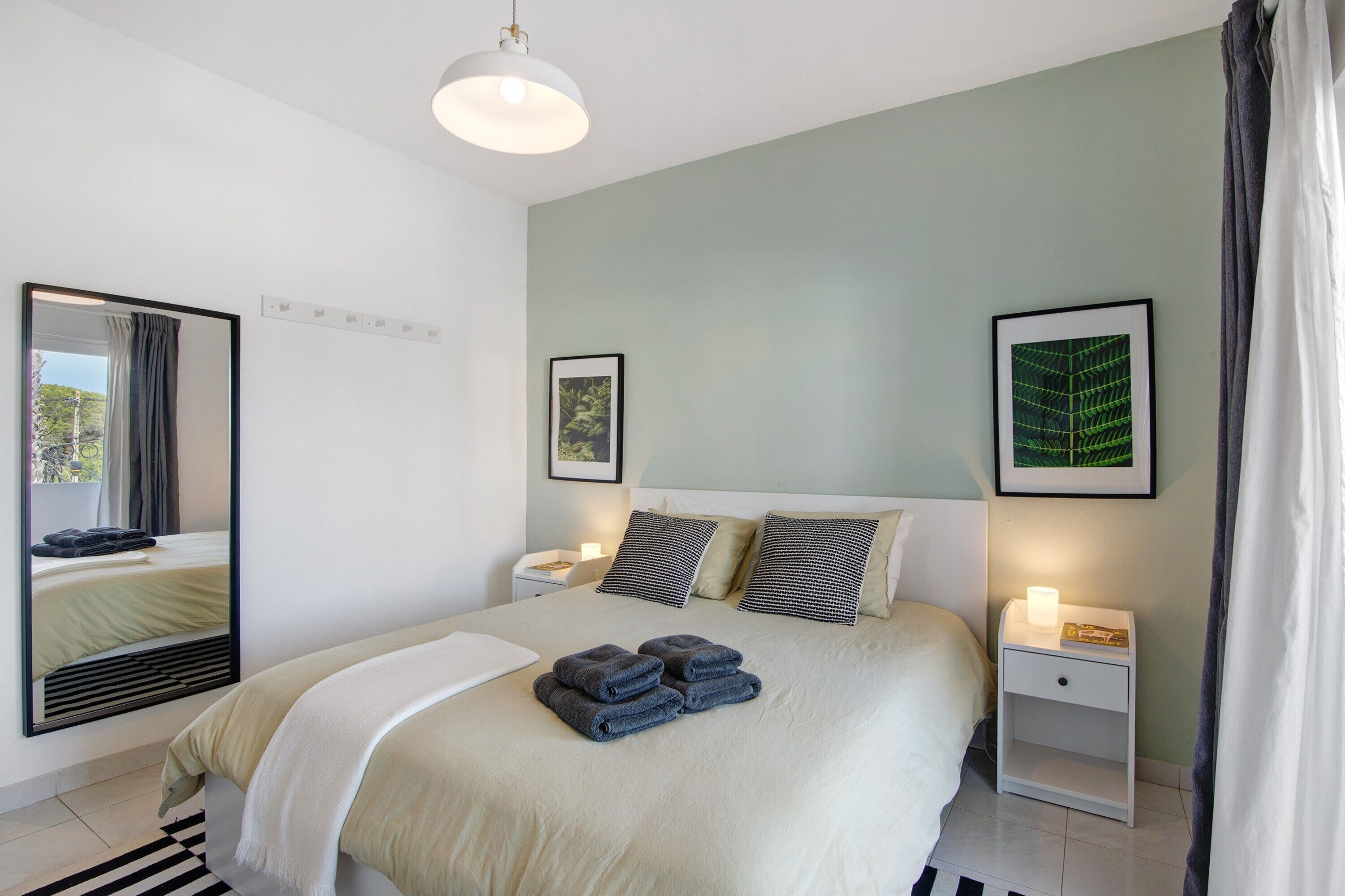 A neatly made bed with folded towels, a bedside table with a lamp, and framed pictures on the wall.