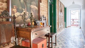Um corredor com chão de azulejos, uma escrivaninha de madeira com gavetas, um quadro na parede e uma porta verde.