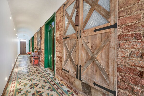 A hallway with a patterned floor, a wooden door with glass panels, and a brick wall.