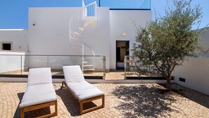 A modern building with a spiral staircase, a tree, and two lounge chairs on a paved patio. - Apartment 'Monte Gerações 4' with Shared Pool, Wi-Fi and Air Conditioning (Almancil)