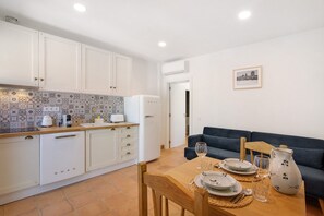 A compact kitchen with white cabinets, a tiled backsplash, and a dining area with a table set for two.