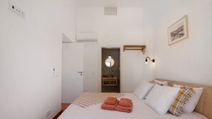 A bedroom with a bed, towels, a wall-mounted light, a framed picture, and a door leading to a bathroom. - Apartment 'Monte Gerações 4' with Shared Pool, Wi-Fi and Air Conditioning (Almancil)