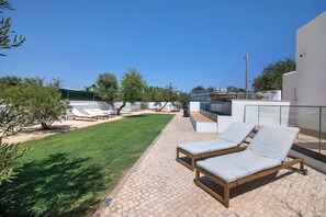 A patio with two lounge chairs, a grassy lawn, and a building with a glass facade.